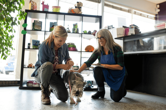 Two woman and a dog kneel in a lobby