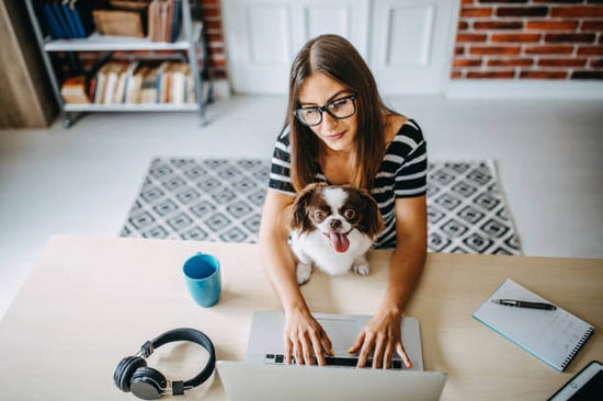 A woman uses a laptop as a dog sits on her lap