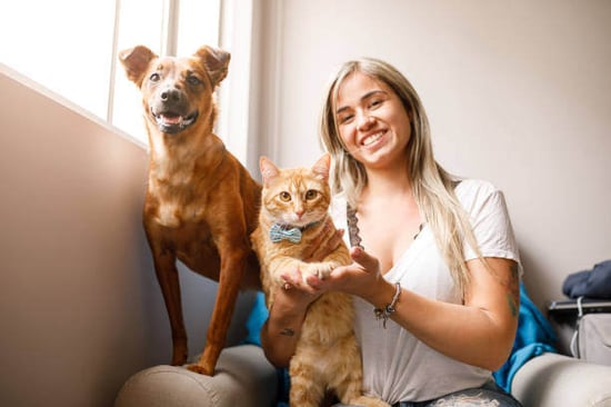 A woman sits with a cat and dog