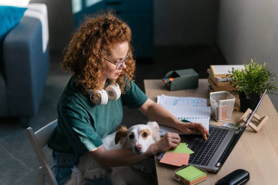 A woman uses a laptop as a dog sits on her lap