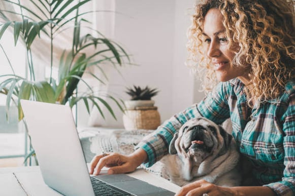 A woman uses her laptop as her dog sits on her lap