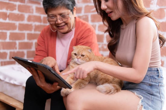 woman teaching older woman how to leave a review on tablet with cat on lap