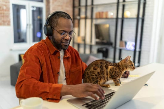 A man uses a laptop as a cat sits next to him
