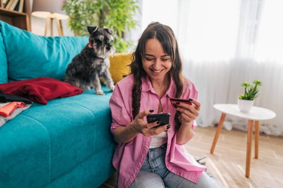 A woman holds a credit card up as a dog sits behind her on the couch